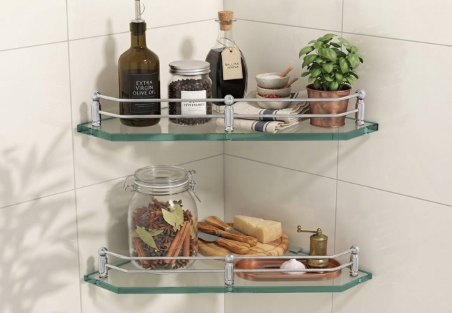 Two glass corner shelves with chrome railings mounted on a tiled wall, holding kitchen bottles, spices, and a plant