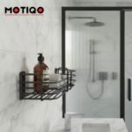 Wall-mounted matte black wire bathroom caddy holding an amber pump bottle and rolled towel on a marble tile wall